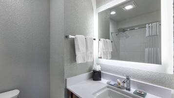 A bathroom with a white sink, a mirror, a towel rack with white towels, and a shower area.