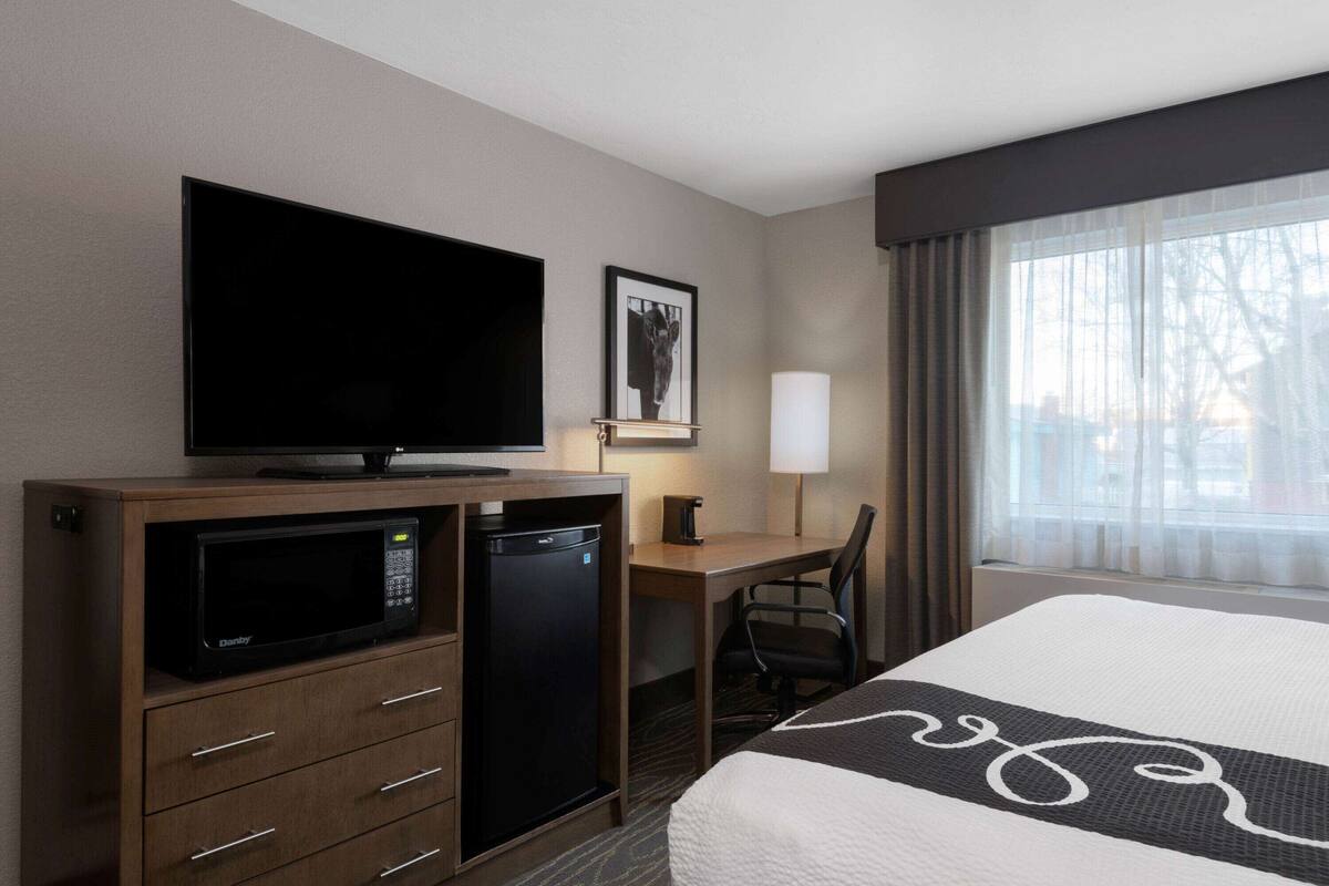 Una habitación de hotel con cama, escritorio con computadora, microondas y televisión.