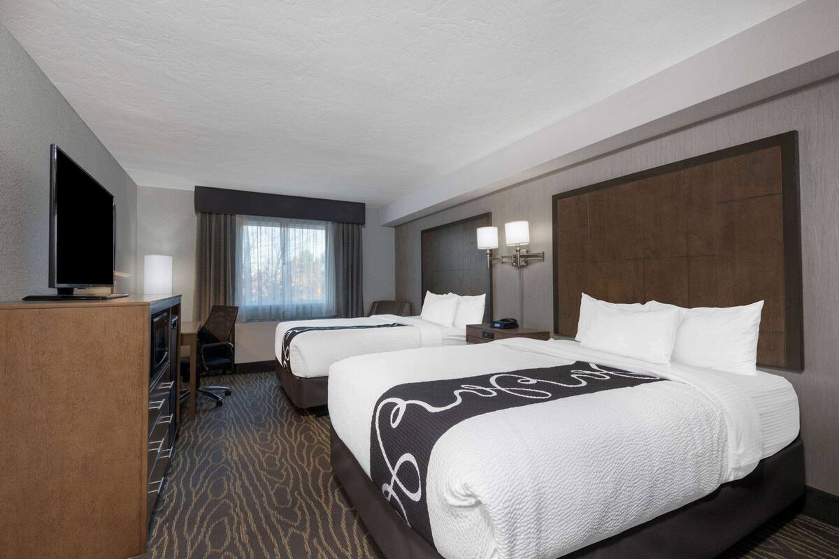 Habitación de hotel con dos camas, televisión, escritorio y ventana con cortinas.