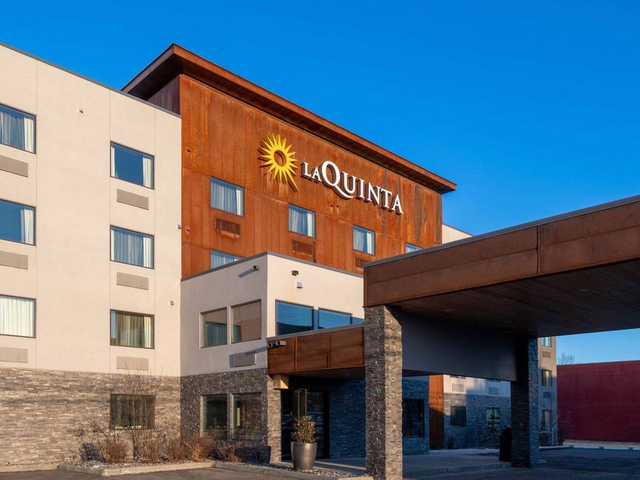 A La Quinta hotel with a modern design, featuring a prominent logo, multiple windows, and a covered entrance area.