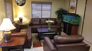A living room with a brown leather sofa, a coffee table, a lamp, a fish tank, and a mirror on the wall.