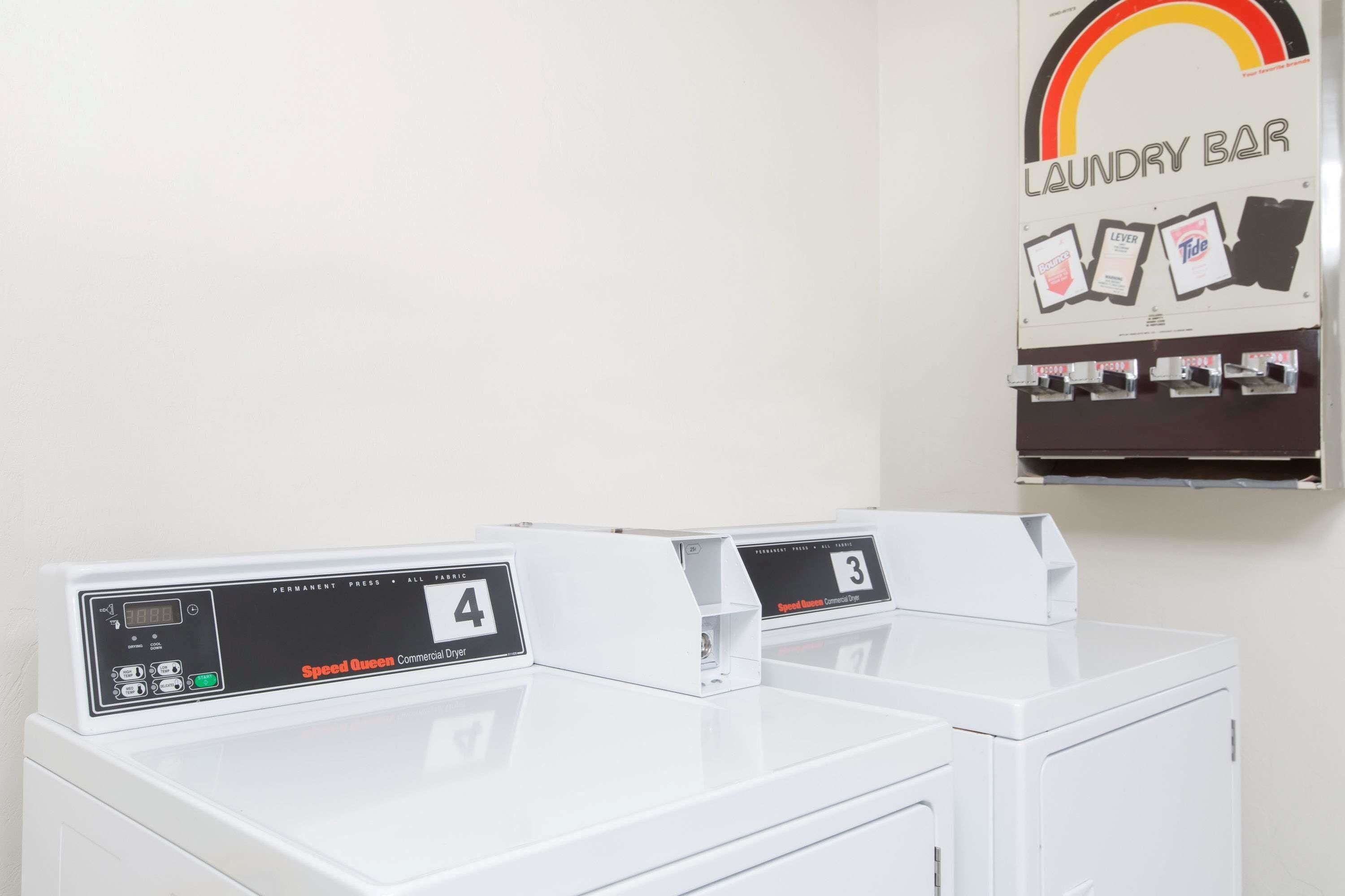 A laundry facility with two Speed Queen dryers, a digital display, and a poster advertising Tide detergent.