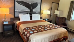 Ein Hotelzimmer mit einem großen Bett, zwei Nachttischen mit Lampen, einem großen Wandbild mit dem Motiv eines Walflossens und Blick auf den Ozean.