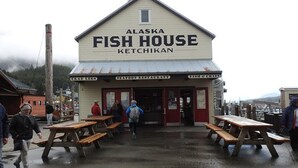 Ein Gebäude mit der Aufschrift "Alaska Fish House Ketchikan", mit Außenbereich und Schildern für "Crab Legs" und "Seafood Restaurant".