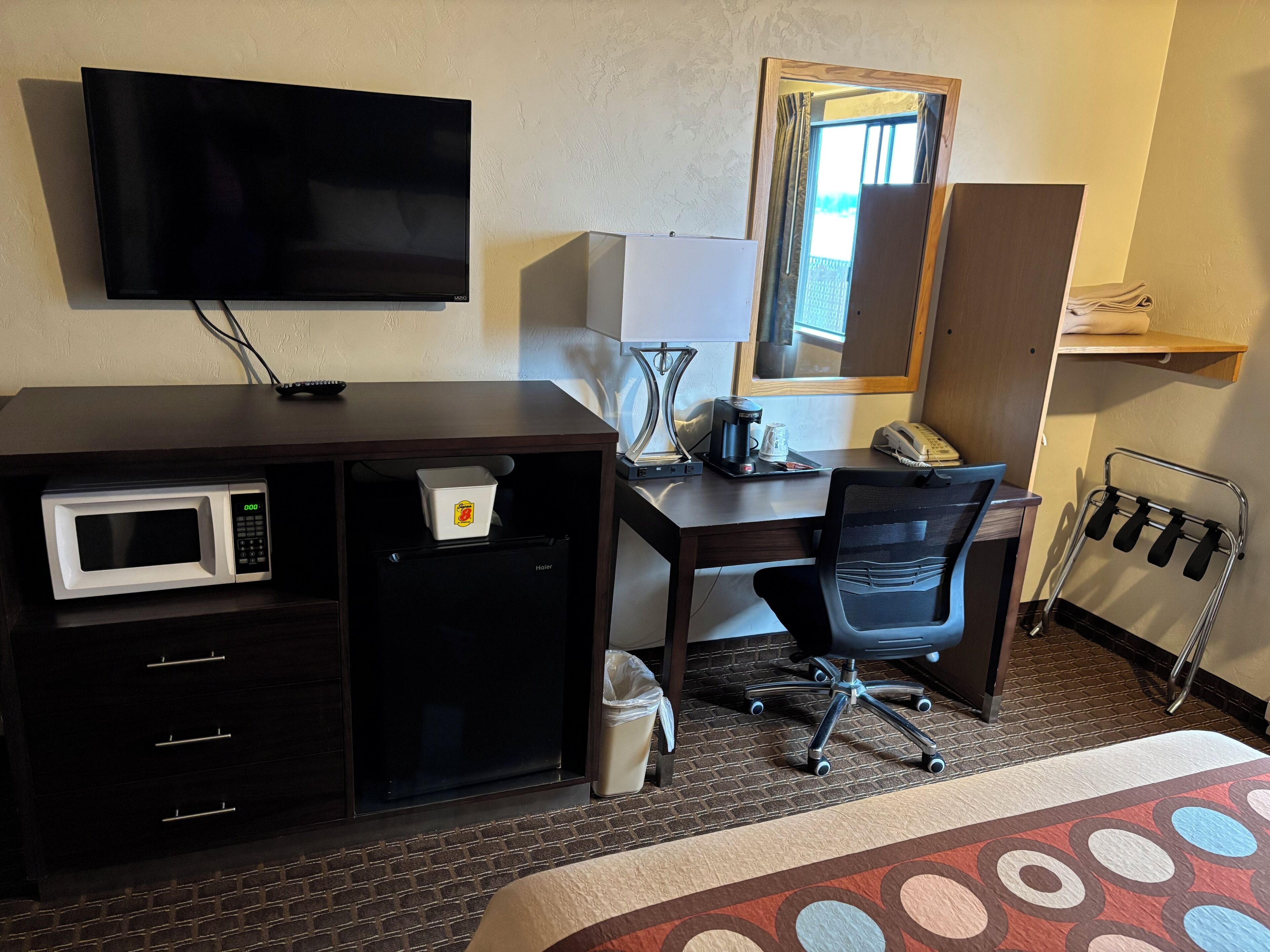 Habitació d'hotel amb un llit, una escriptori amb una cadira, microones, nevera, televisió, cafetera i un telèfon.
