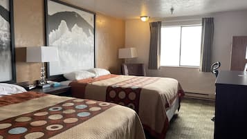 Une chambre d’hôtel avec deux lits, un bureau, une chaise, une lampe, une fenêtre avec des rideaux et un tableau au mur.