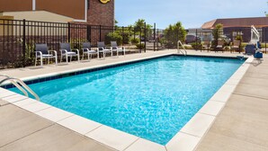 A rectangular swimming pool with a tiled edge, surrounded by lounge chairs and a fence.