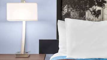 Een hotelkamer met een bed, een nachtkastje met een lamp en een wand met een ingelijst schilderij.