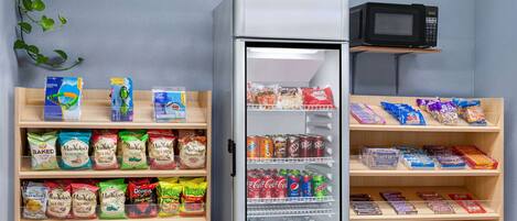A vending machine stocked with snacks and drinks, a microwave above it, and shelves with packaged goods.