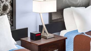 A neatly made bed with a blue and brown blanket, a bedside table with a lamp, a radio, and a drawer.