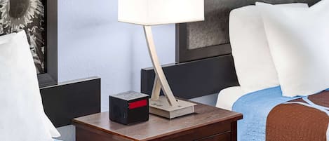 A neatly made bed with a blue and brown blanket, a bedside table with a lamp, a radio, and a drawer.