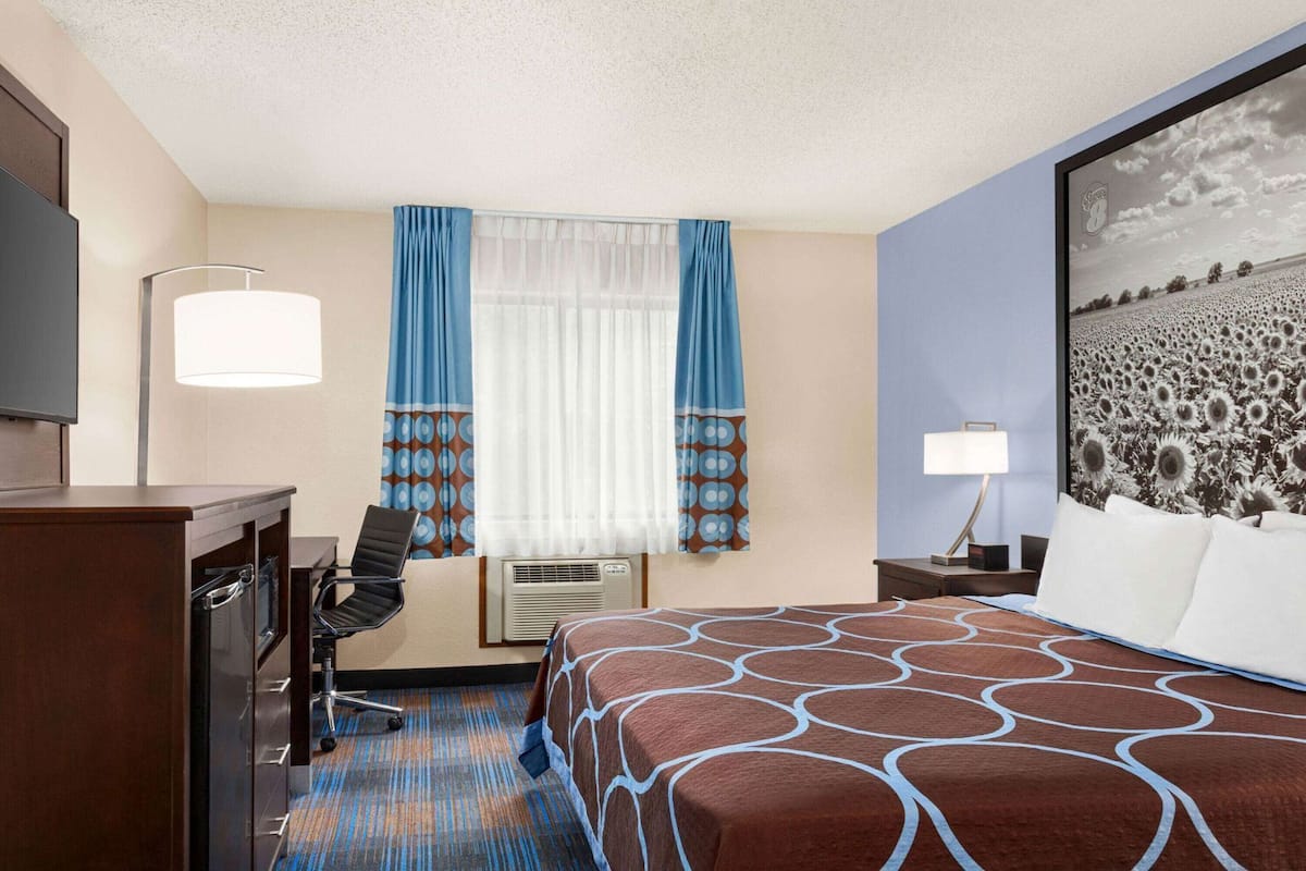A hotel room with a bed, desk, chair, and a large window with curtains.