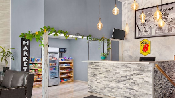 A modern reception area with a stone counter, a 'Super 8' sign, a 'MARKET' sign, and a 'GREETINGS' framed picture.