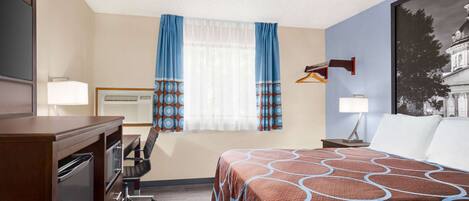 Quarto de hotel com cama, escrivaninha, cadeira e luminária na parede.