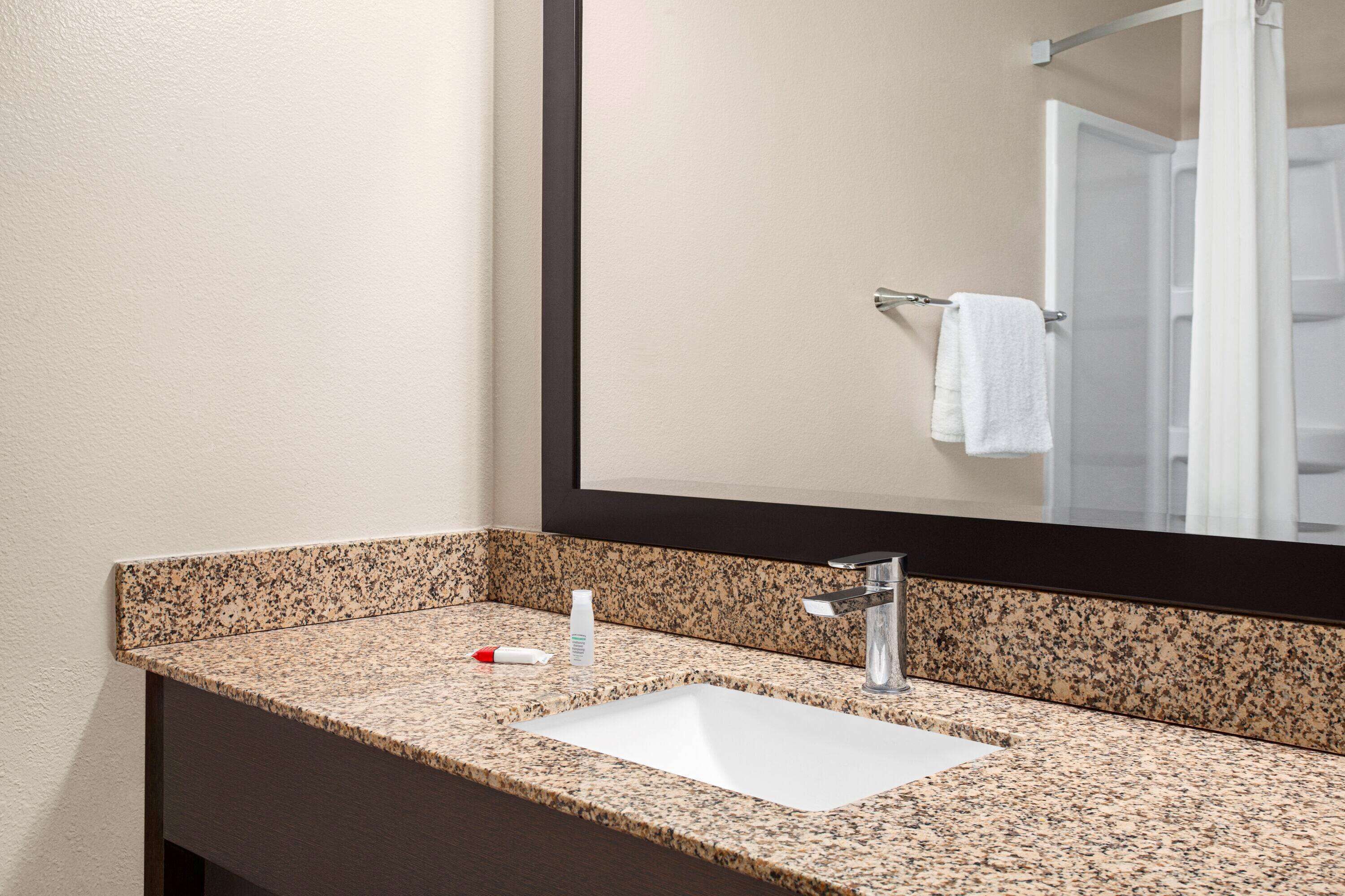 A bathroom with a granite countertop, a white sink, and a large mirror.