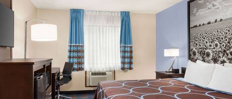 A hotel room with a bed, desk, chair, and a large framed picture on the wall.