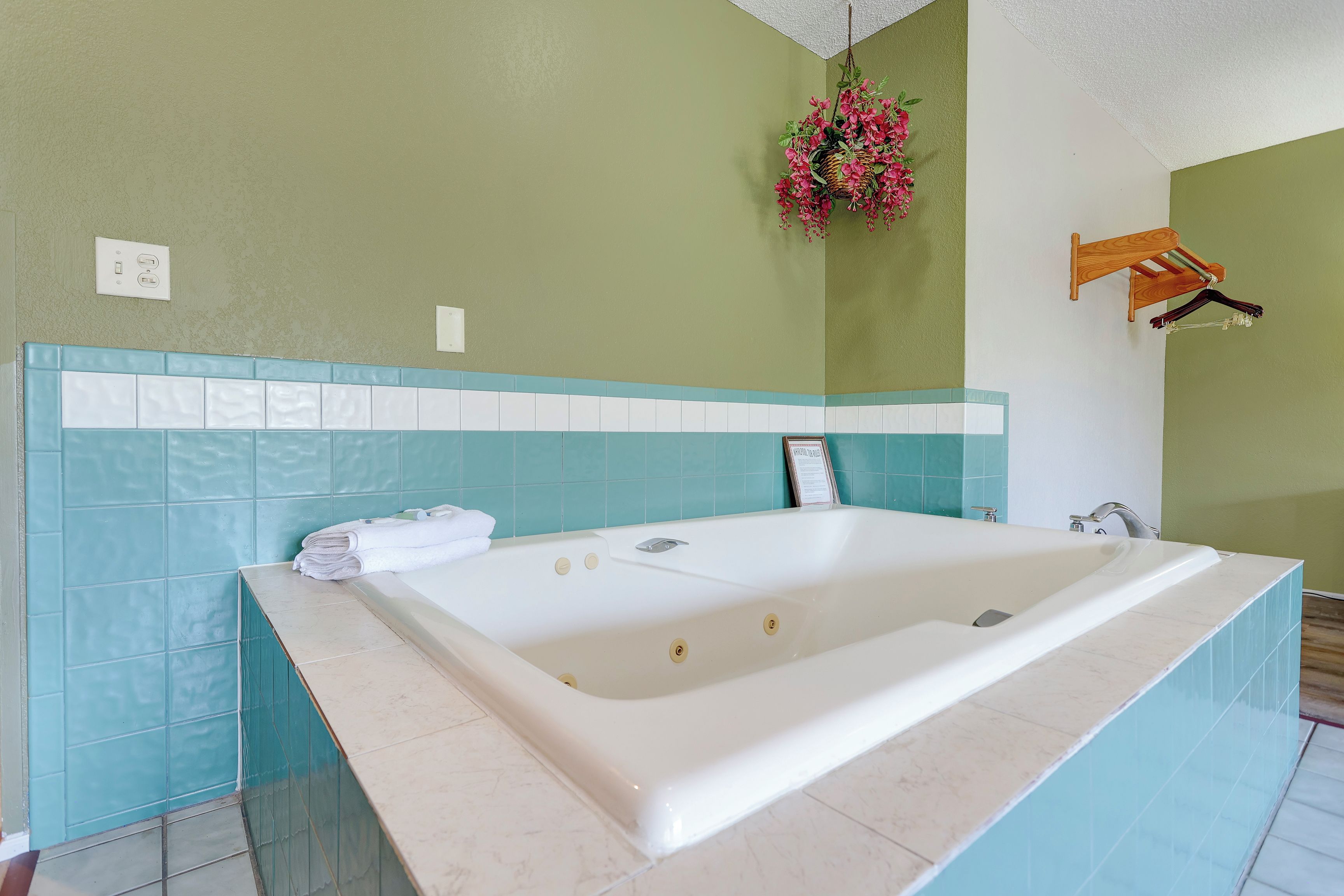 Une salle de bain avec une grande baignoire, des murs verts et une décoration florale suspendue.
