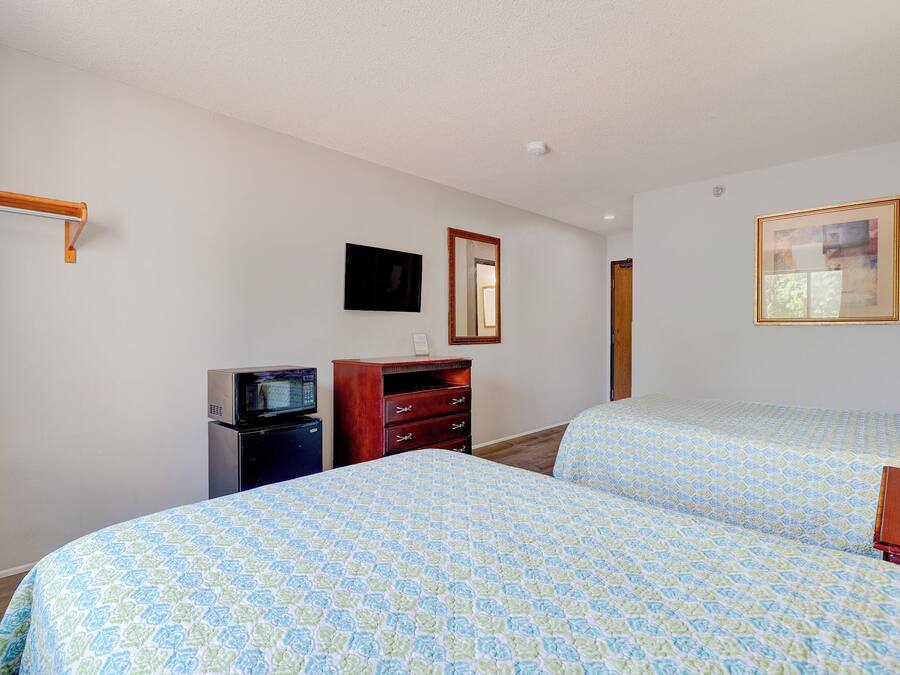 Una habitación de hotel con dos camas, un aparador, un televisor y un espejo.