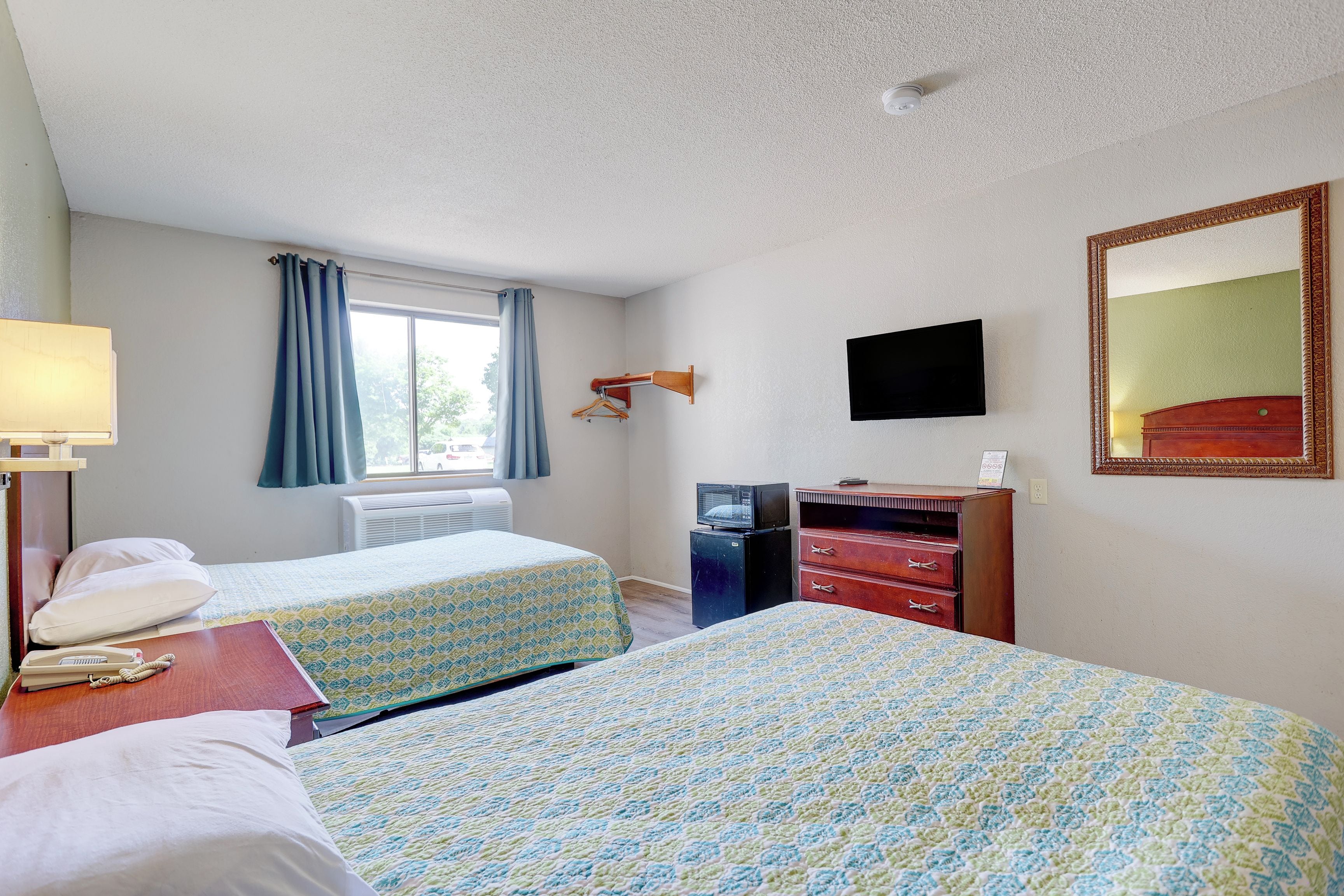 Une chambre d’hôtel avec deux lits, une télévision, une commode et une fenêtre avec des rideaux.