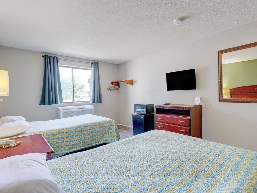Une chambre d’hôtel avec deux lits, une télévision, une commode et une fenêtre avec des rideaux.