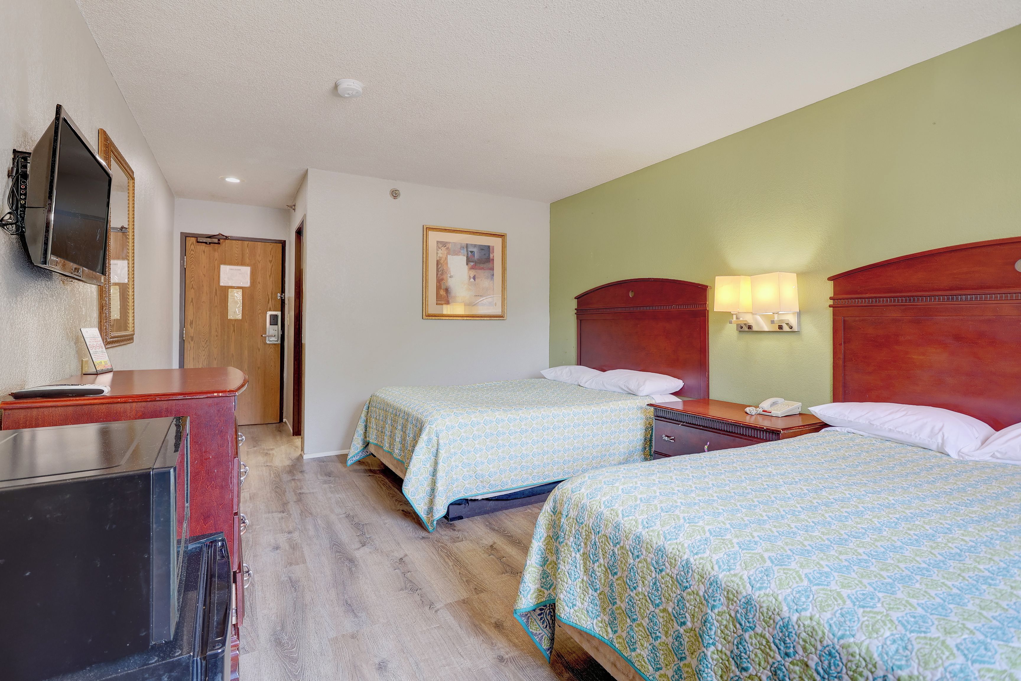 Een hotelkamer met twee bedden, een bureau met een televisie, een deur en een fotokader aan de muur.