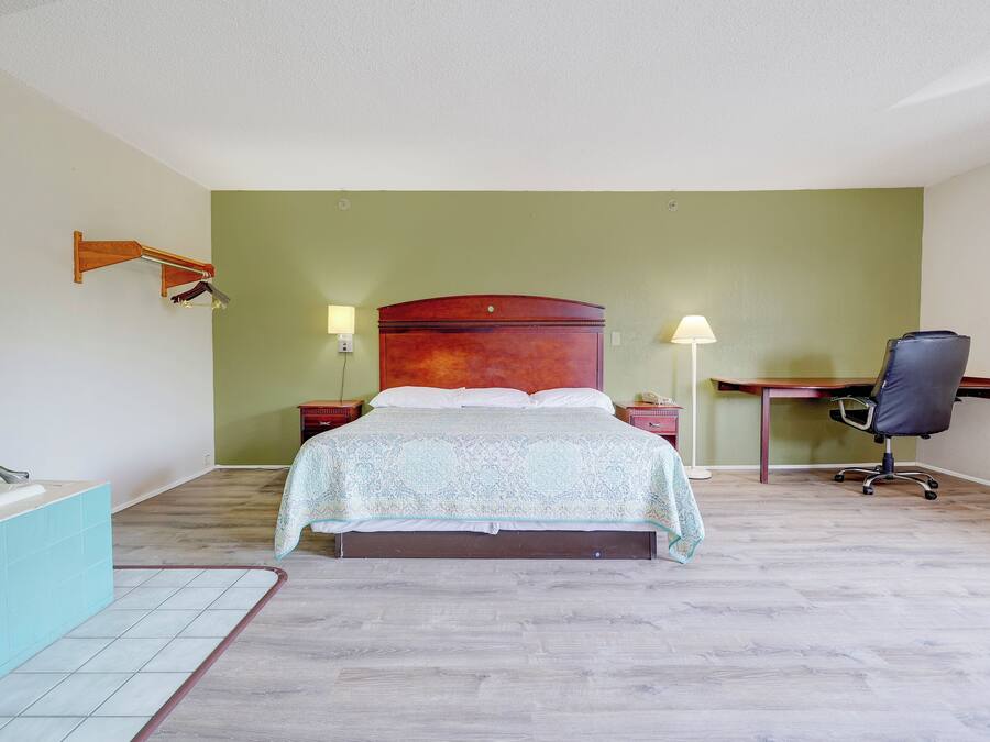 A bedroom with a bed, a desk, a chair, a nightstand, and a lamp.