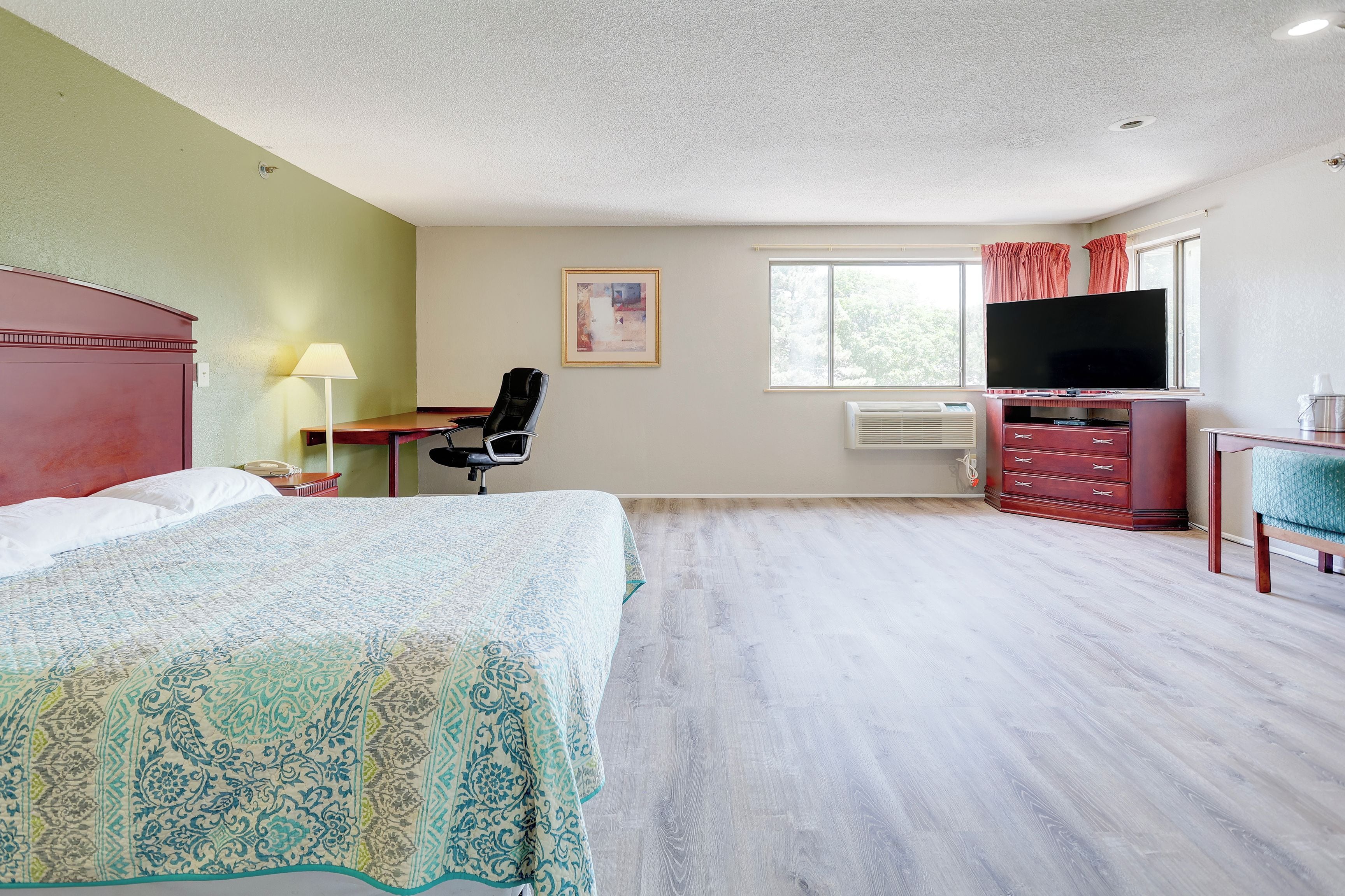 A hotel room with a bed, desk, chair, television, and a window with curtains.