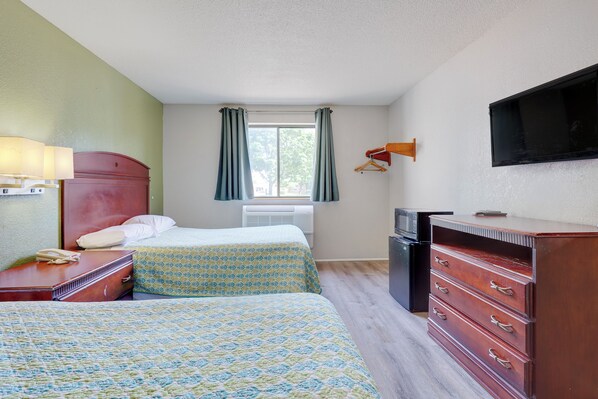 A hotel room with two beds, a desk, a dresser, a TV, and a window with curtains.