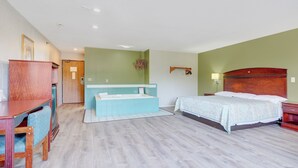 A hotel room with a wooden desk, a large bed, a bathroom with a bathtub, and a green wall. - Coldwater Inn & Suites near I 69 (Coldwater)