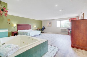 Habitación de hotel con una bañera grande, dos camas, un escritorio y un ventanal.