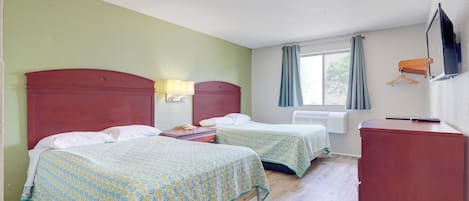Habitación de hotel con dos camas, un escritorio, una silla, televisión y ventana con cortinas.