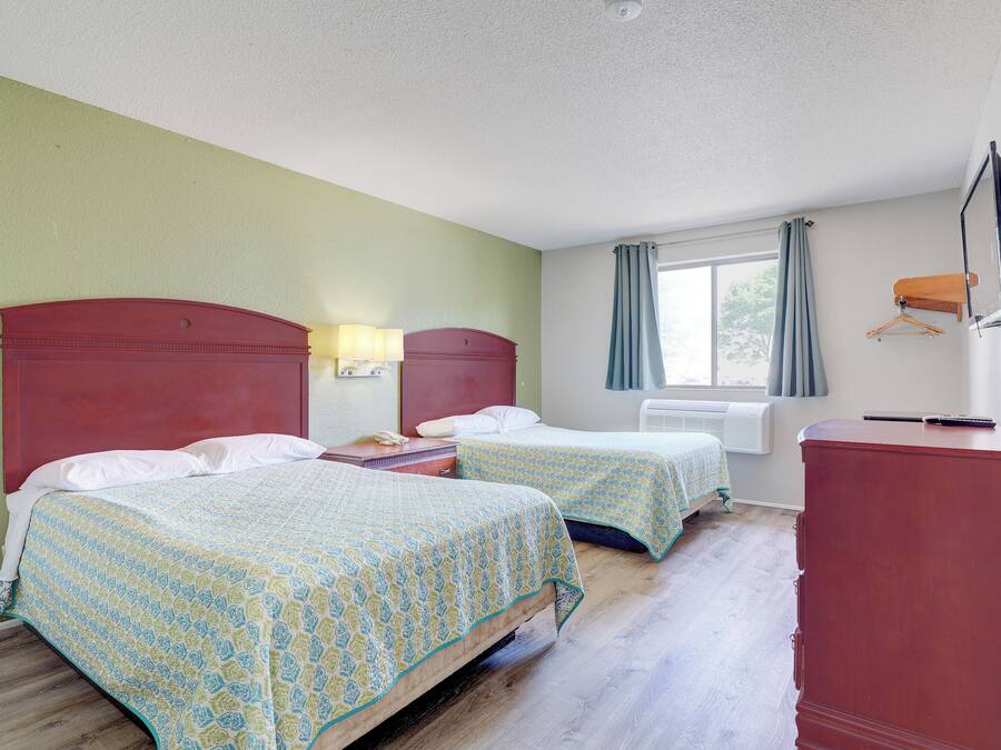 Een hotelkamer met twee bedden, een bureau, een stoel, een televisie en een raam met gordijnen.