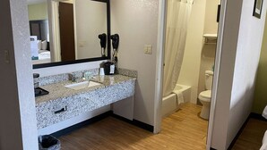 A bathroom with a granite countertop sink, a mirror, hair dryers, a shower curtain, and a toilet. - Motel 6 Lancaster, PA (Lancaster)