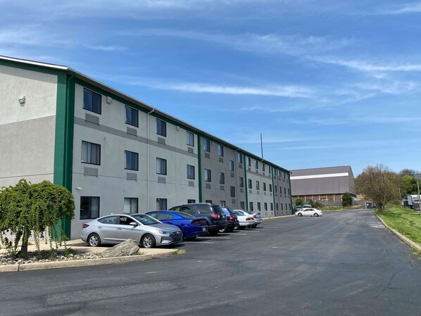 Un parking où plusieurs voitures sont garées devant un immeuble à étages dont la façade est agrémentée d’une couleur verte.