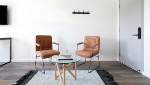 A modern living room with a glass coffee table, two leather armchairs, a mounted TV, and a door with a black handle. - Motel 6 Lancaster, PA (Lancaster)