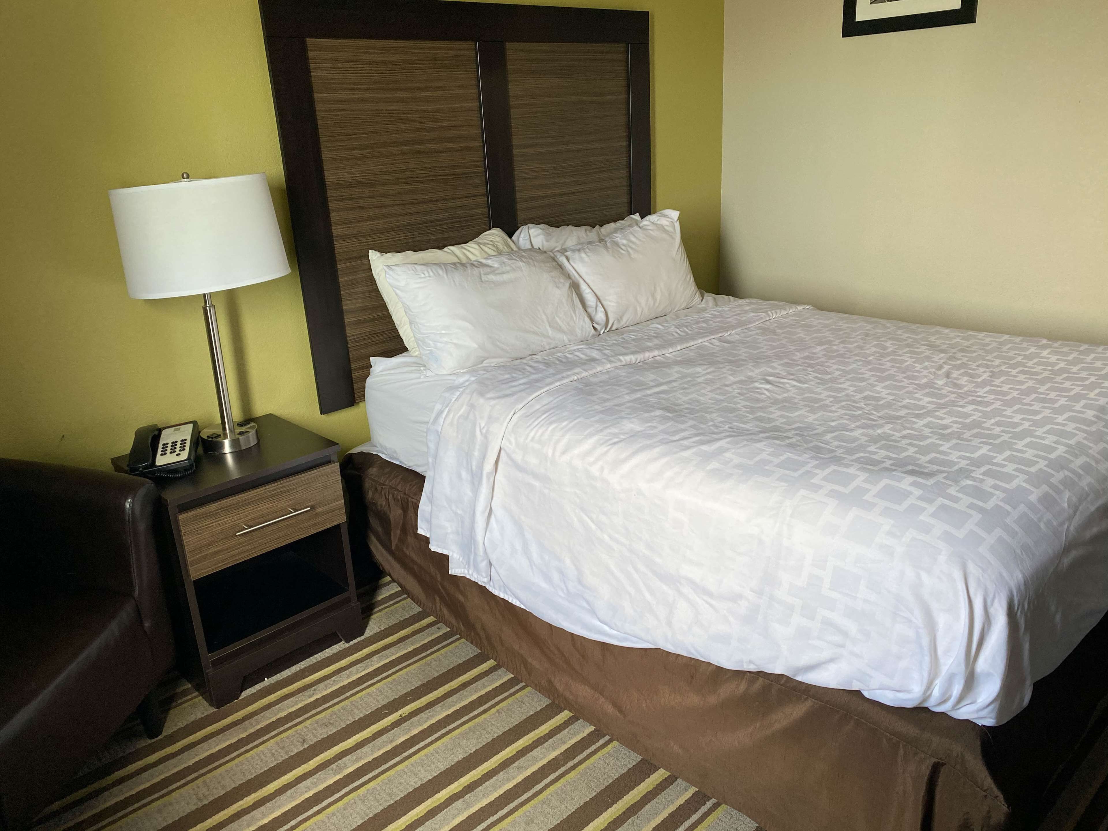 A hotel room with a bed, a nightstand with a lamp, a phone, and a brown leather chair.