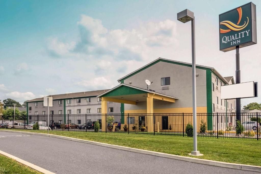 Ein Quality Inn Hotel mit überdachtem Eingang, einem eingezäunten Parkplatz und blauem Himmel.