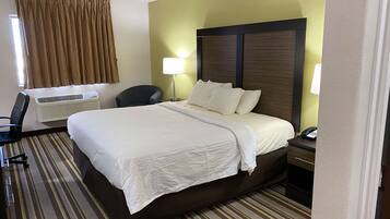 A hotel room with a large bed, a desk, a chair, a lamp, and a telephone.