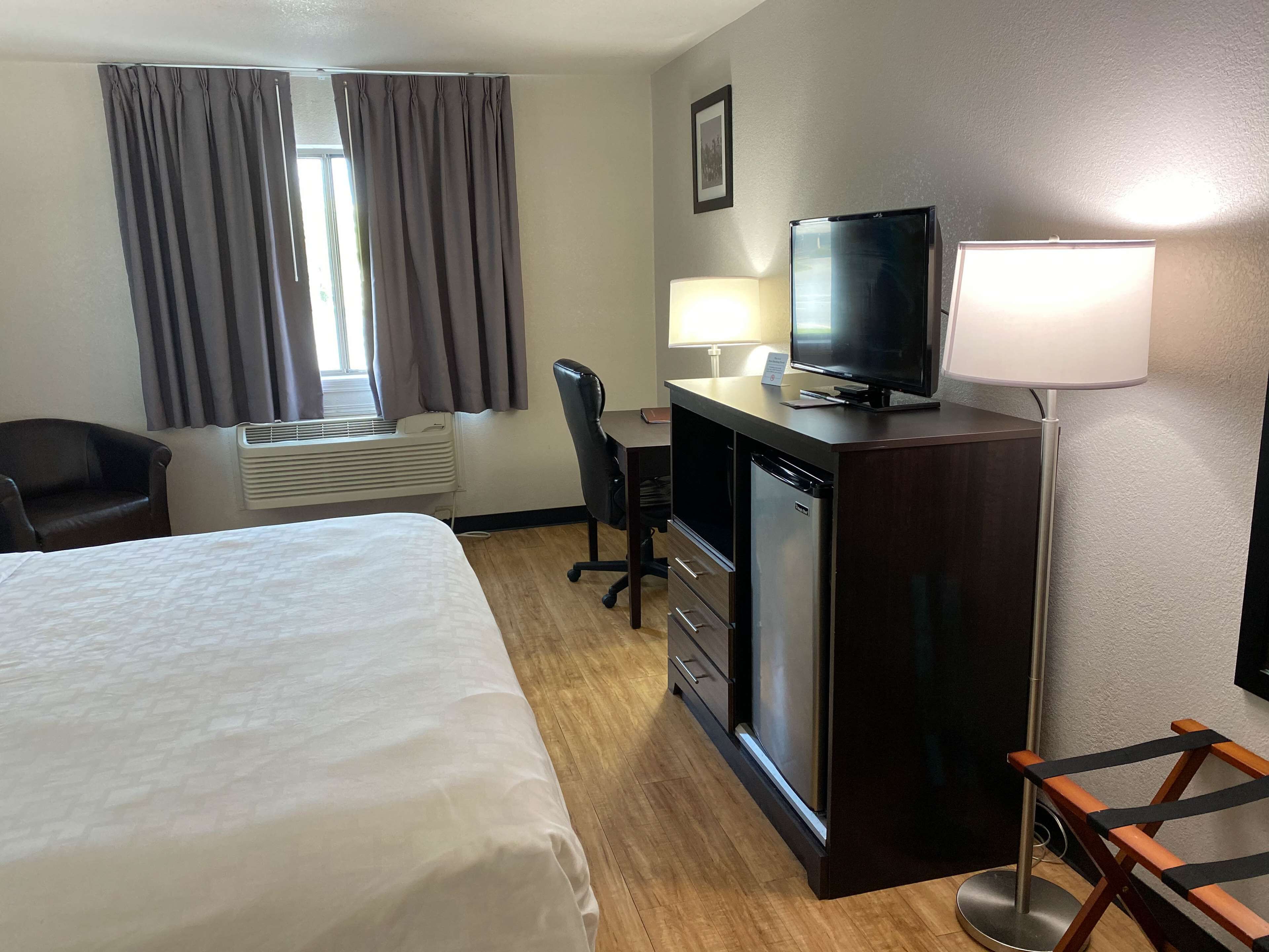 A hotel room with a bed, desk, television, and a chair.