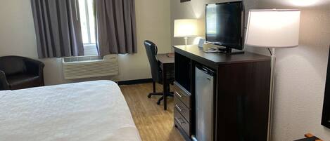 A hotel room with a bed, desk, television, and a chair.