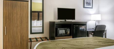 A hotel room with a bed, a television, a microwave, a refrigerator, a desk with a chair, a wardrobe, and a mirror.