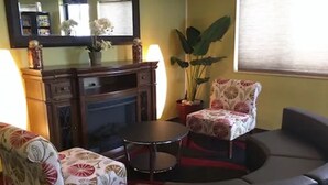 A living room with a fireplace, a sofa, a chair, and a table. - Motel 6 Lancaster, PA (Lancaster)