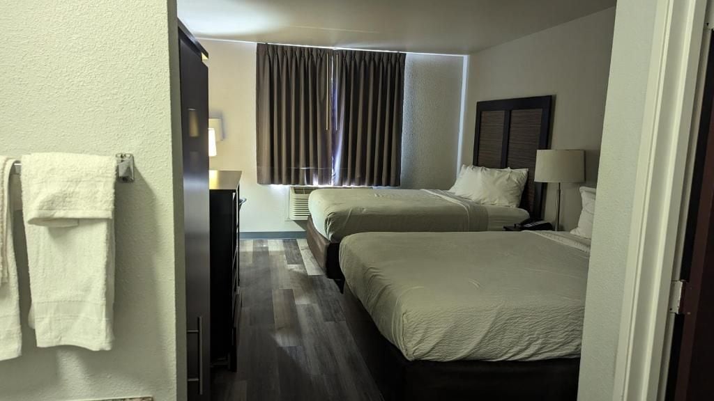 Una habitación de hotel con dos camas, una ventana con cortinas, una lámpara y un perchero para toallas.