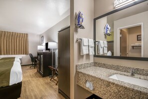 Une chambre d’hôtel équipée d’un lit, d’un bureau, d’une chaise et d’un grand miroir au-dessus du lavabo.