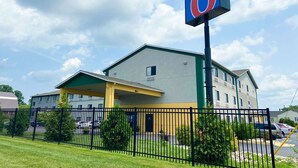 A motel with a large '6' sign, a covered parking area, and a fenced parking lot. - Motel 6 Lancaster, PA (Lancaster)
