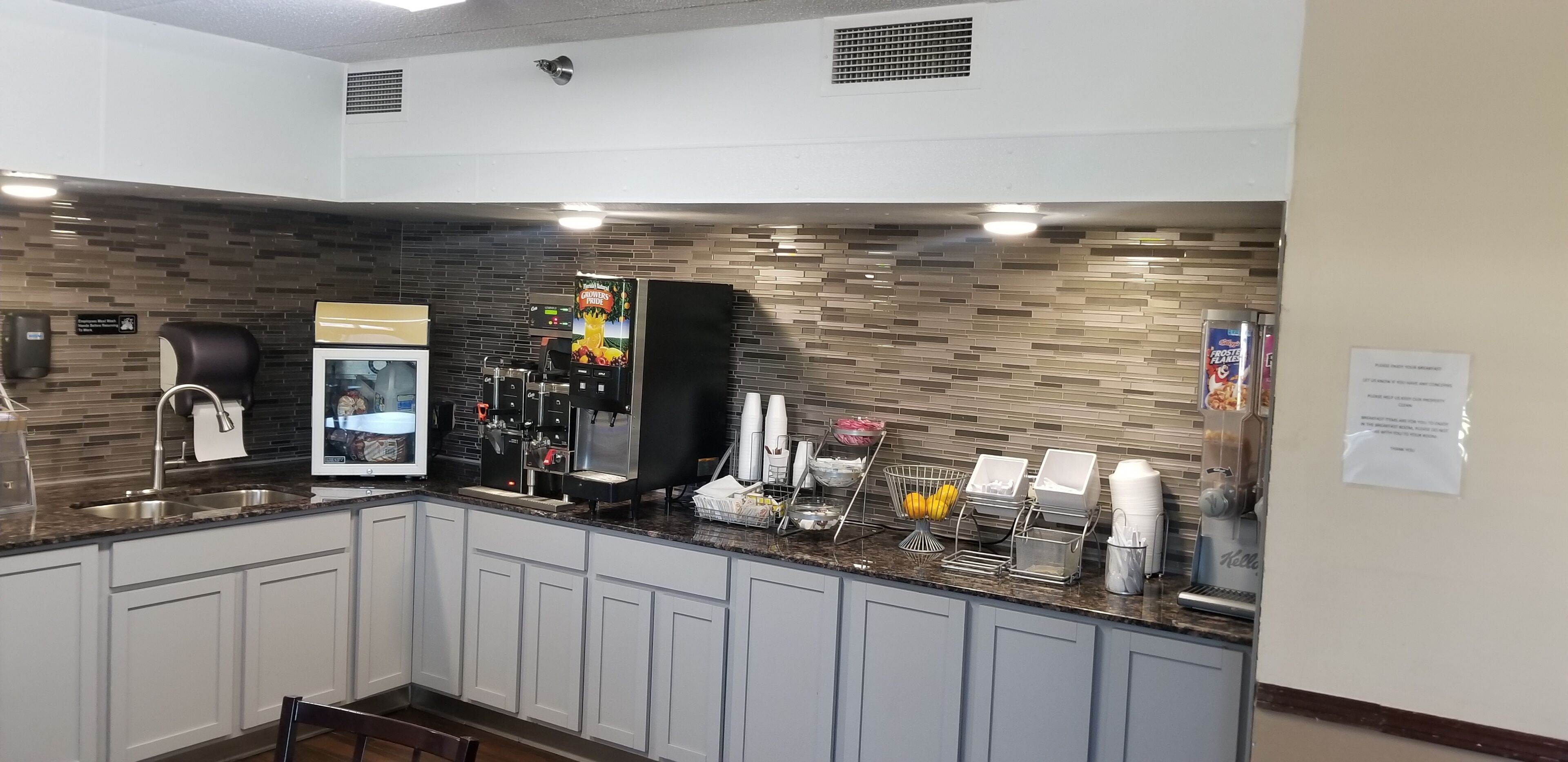Een moderne keuken met een betegelde spatwand, een koffieapparaat en een drankenspender.