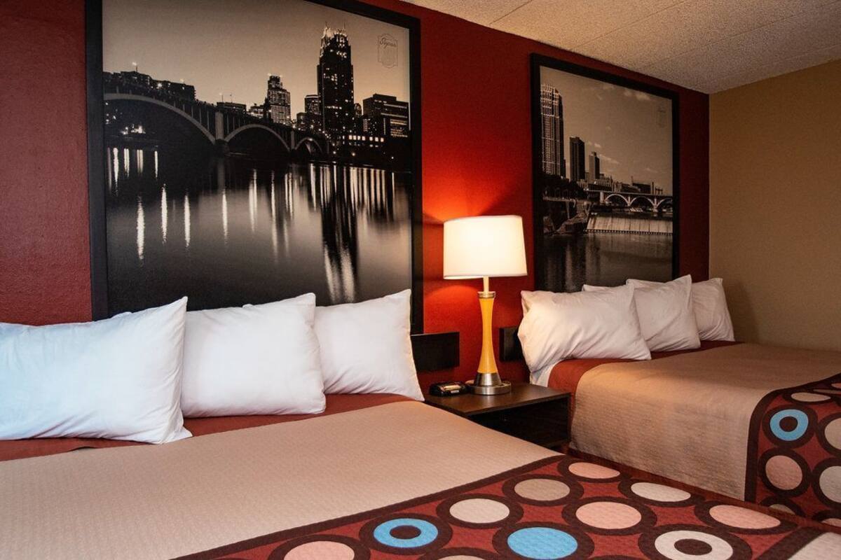 Une chambre d’hôtel avec deux lits, une table de chevet avec une lampe et deux grandes affiches représentant des paysages urbains accrochées aux murs.