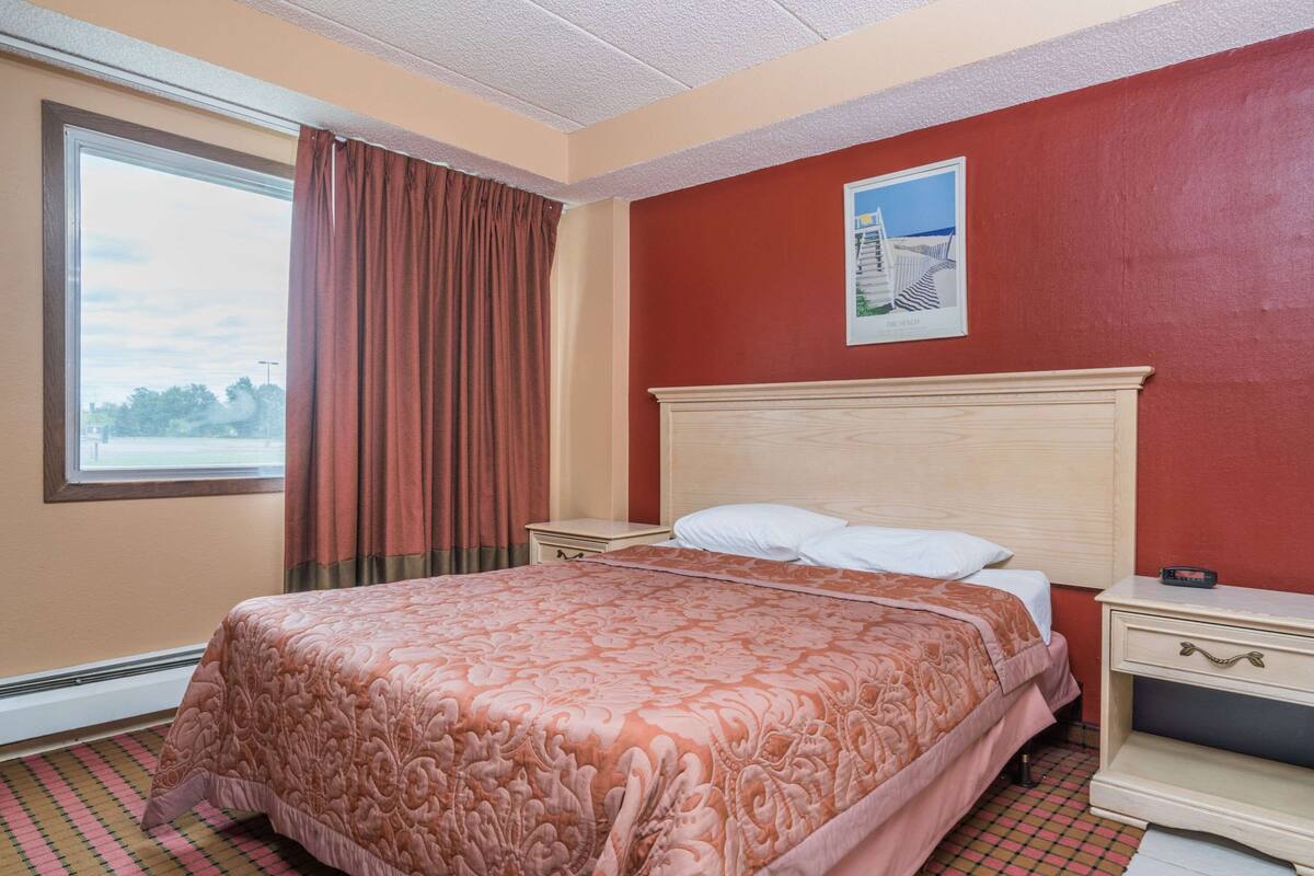 Une chambre d’hôtel avec un grand lit, une table de chevet, une commode et une fenêtre avec des rideaux.