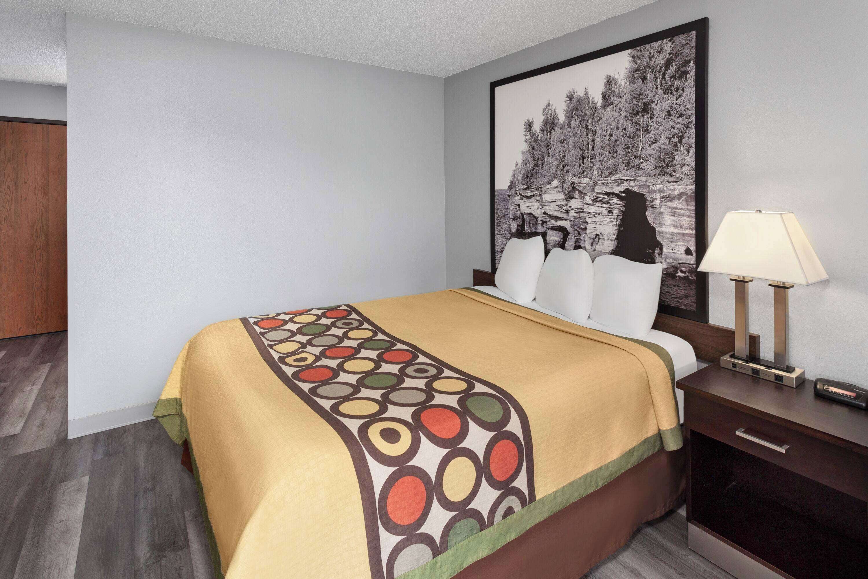 A hotel room with a bed, a nightstand, a lamp, and a painting on the wall.