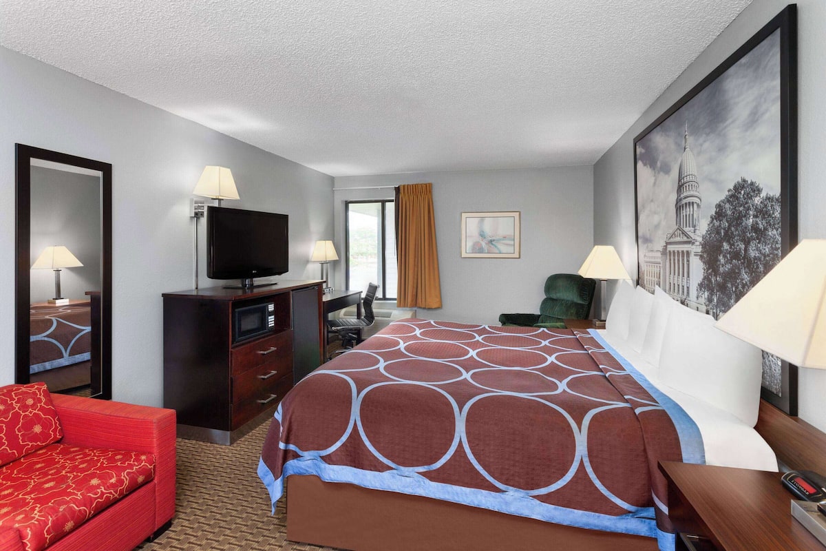 A hotel room with a large bed, a red sofa, a desk with a TV, and a painting on the wall.